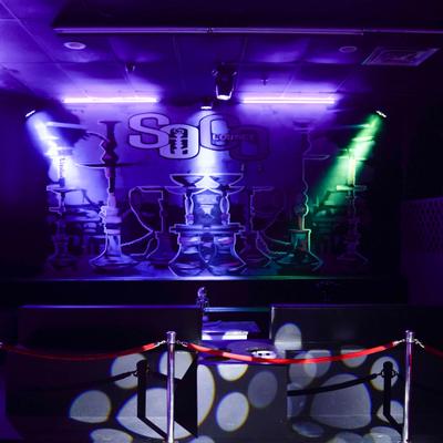 Hookah lounge stage with purple and green lighting and velvet rope barrier.