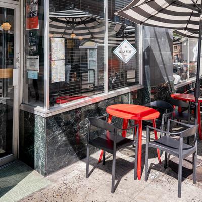 Entrance and outdoor seating area with red tables, black chairs, and striped parasols.
