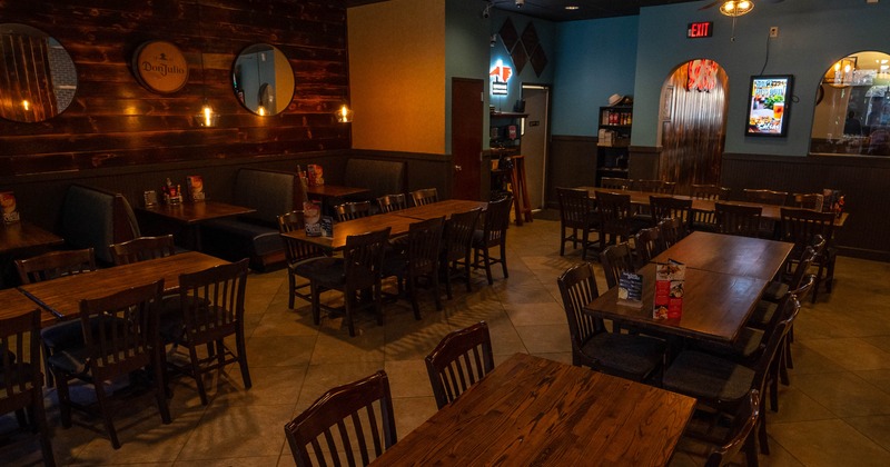 Restaurant interior with wooden tables, booths, and chairs and warm lighting.