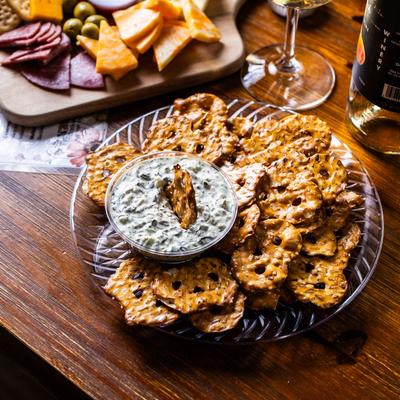 Pretzel chips and spinach dip with wine and a charcuterie board in the background.