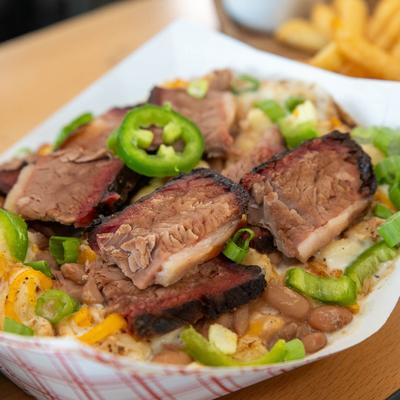 A takeout Mac N Cheese bowl with sliced brisket.