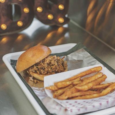 Pulled pork sandwich, served on a tray with fries, side view.