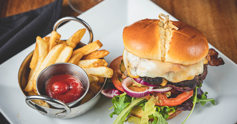 Burger with melted cheese, bacon, lettuce, tomato, and onion, a side of French fries and ketchup