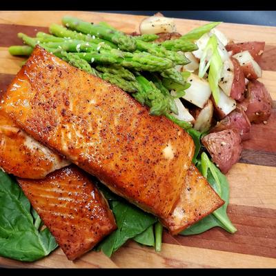 Grilled salmon fillets served with roasted potatoes and asparagus on a wooden board.