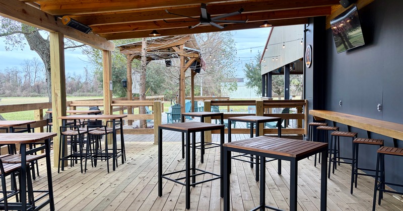 Open patio area with tall tables overlooking a grassy yard and wooden pergola