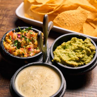 Tortilla chips accompanied by cheese sauce, guacamole, and corn salsa.