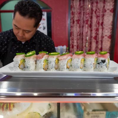 Sushi roll plate on sushi bar counter, with an employee behind it.