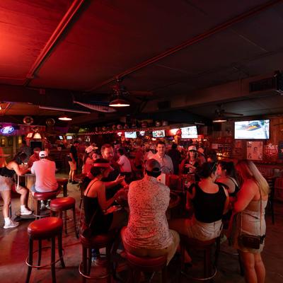 Crowded bar with people socializing under red lighting.