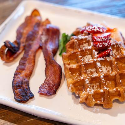 Two Belgian waffles topped with whipped butter and syrup, served with applewood smoked bacon or fruit.
