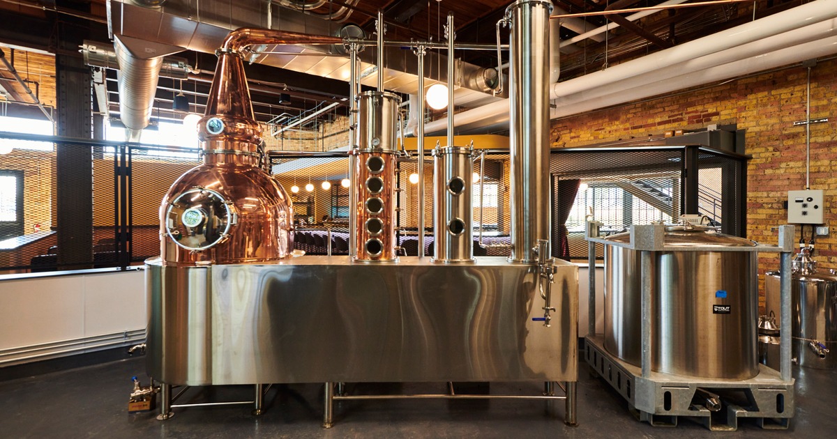 Copper still and stainless steel distilling equipment inside modern industrial distillery