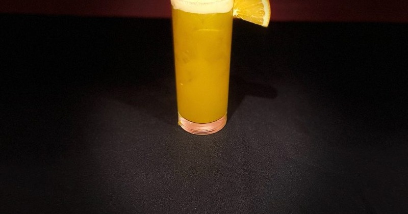 A cocktail garnished with a fresh orange slice, placed on a black table surface