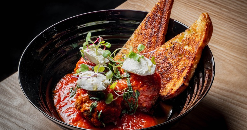 Meatballs in red sauce served in a dark bowl with garlic bread