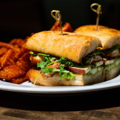 Fried chicken sandwich on toasted ciabatta bread with a side of sweet potato fries.