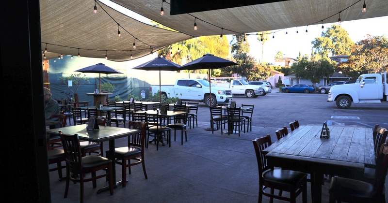 Outdoor patio with tables, umbrellas and string lights, adjacent to a parking lot with trucks