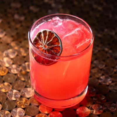 Red cocktail served in rocks glass, garnished with dried lime wheel.