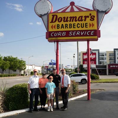 Exterior, group picture by the signage, 3rd and 4th generations of Doumar family.