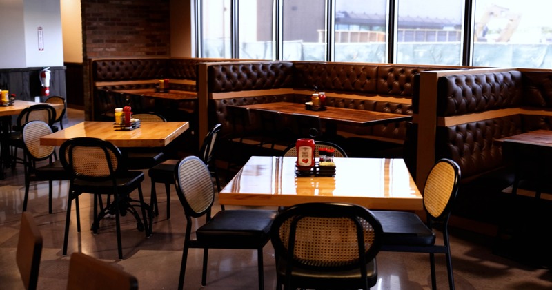Restaurant interior with wooden tables, black chairs, and leather booths