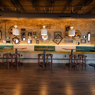 Interior, tables and bar stools by a wall decorated with mirrors and frames.