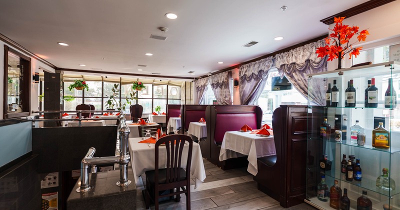 Interior seating area with tables set with white cloths and maroon leather booths