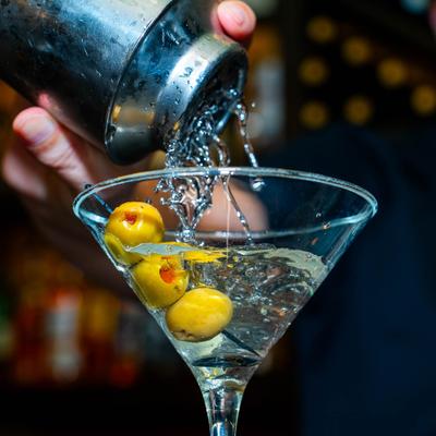 Cocktail being strained into a martini glass with olives.