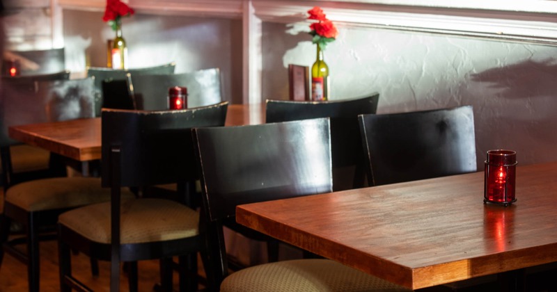 Interior, closeup of lined up tables decorated with flowers and lit candle lamps