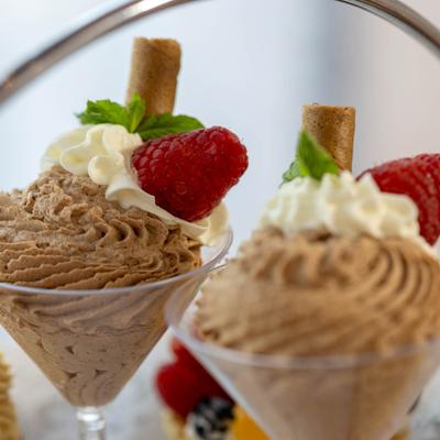 Chocolate mousse topped with whipped cream, raspberry, mint leaf, and a wafer stick.
