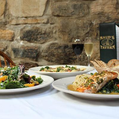 Grilled salmon, pasta, and a salad served with wine on a table against a stone wall.
