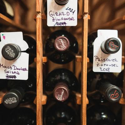 Red wine bottles in a wooden rack, some of them labeled with grape variety and vintage.