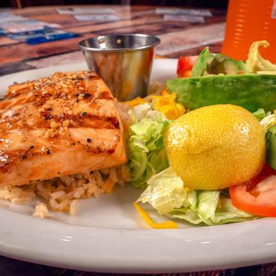 Grilled salmon served with rice, salad, lemon wedges and sauce.