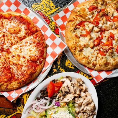Two pizzas and a dinner salad on a colorful table.