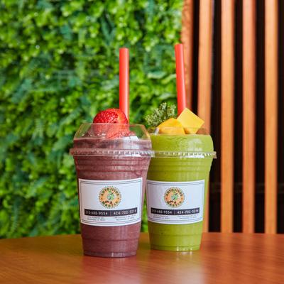 Two fruit smoothies in branded plastic cups on a table.