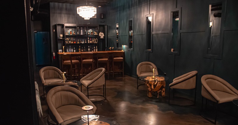 Interior, lounge area, comfortable armchairs with low tables, bar with stools in the back