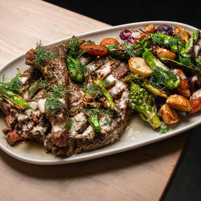 Bone-in Ribeye served on a oval plate with roasted vegetables and baby potatoes.