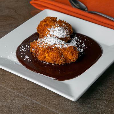 Sweet fritters dusted with powdered sugar over chocolate sauce.