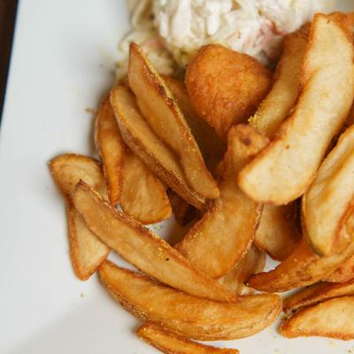 Fried fish served with potato wedges and coleslaw, close-up.