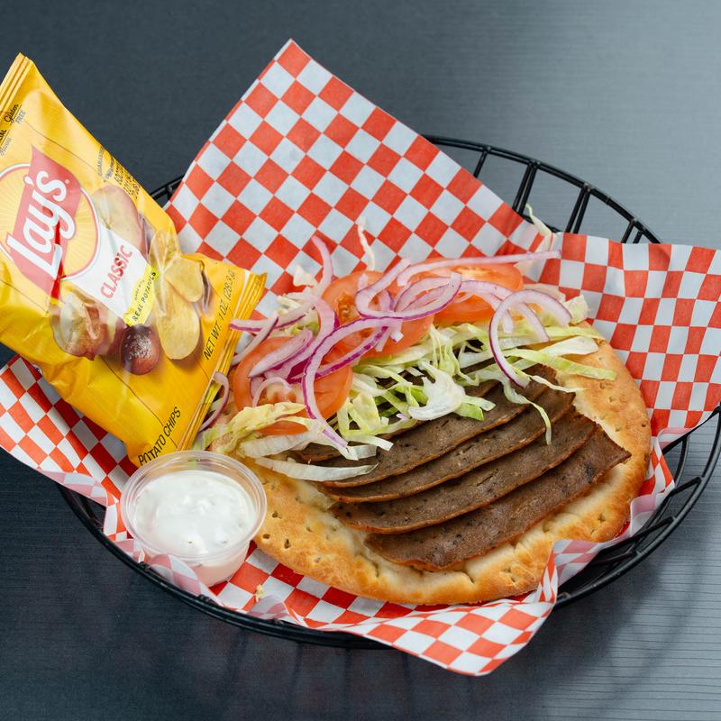 Greek gyro with lamb, lettuce, tomatoes, red onion, tzatziki, and a bag of  potato chips.
