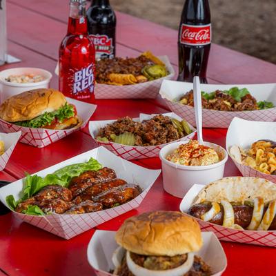 An assortment of food plates and drinks spread on a table outside.