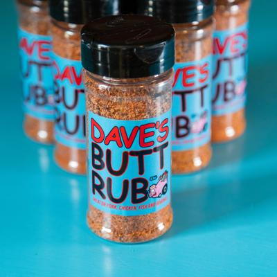 Several bottles of Dave's Butt Rub seasoning are arranged on a bright blue surface.