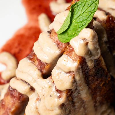 Stuffed French toast drixxled with sauce and garnished with mint leaf, close-up.