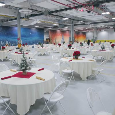 Christmas banquet hall setup with round tables, red napkins, and festive decorations.