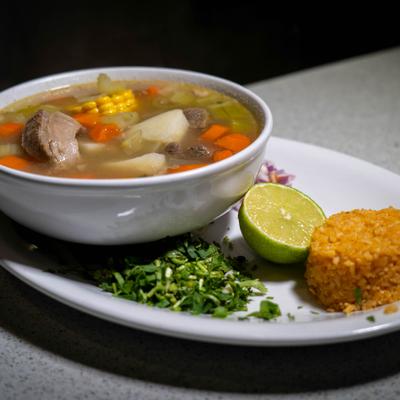 Caldo de Res bowl with rice, red onion, cilantro, and lime on the side.
