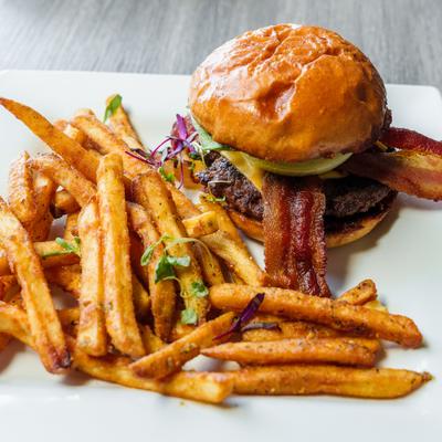 Bacon cheeseburger and seasoned fries on a white plate.