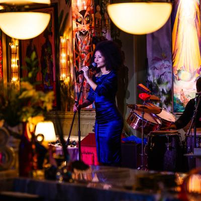 Singer performing at Calle Dragones with colorful painting in the background.