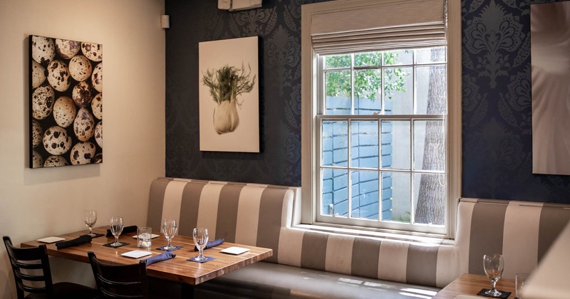 Set dining tables and banquette seating by a window, pictures on walls