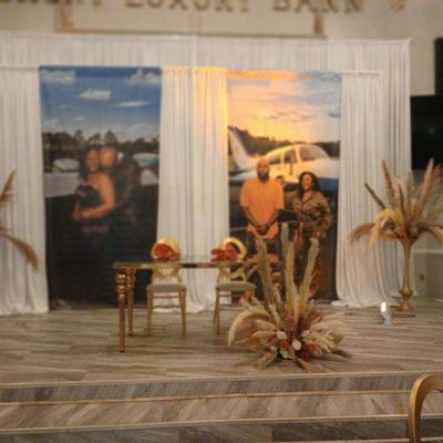 A decorated stage features customized picture backdrops, white curtains, and floral arrangements.