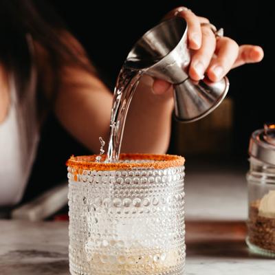 A hand pouring a cocktail into a glass.
