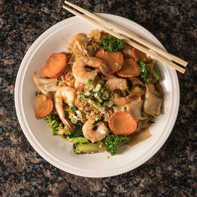 Shrimp stir-fry noodles with vegetables on a white plate with chopsticks.