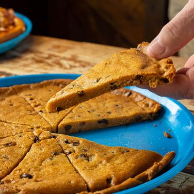 A hand lifting a slice of chocolate chip pizza from the pie.