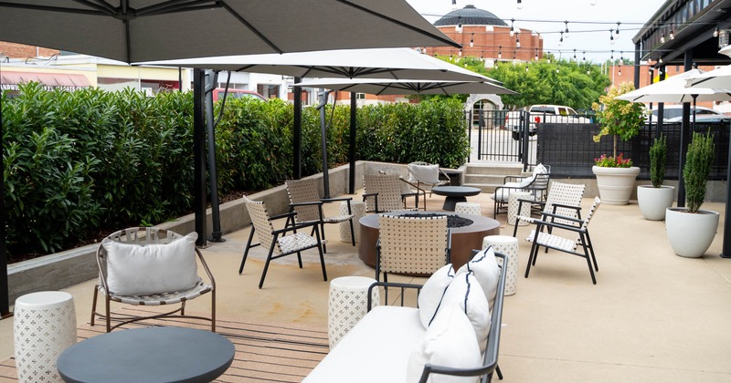 Outdoor seating area, tables, chairs, large umbrellas, greenery and ambient string lights