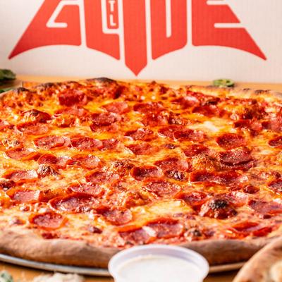 Pepperoni pie with restaurant's wall logo in the background